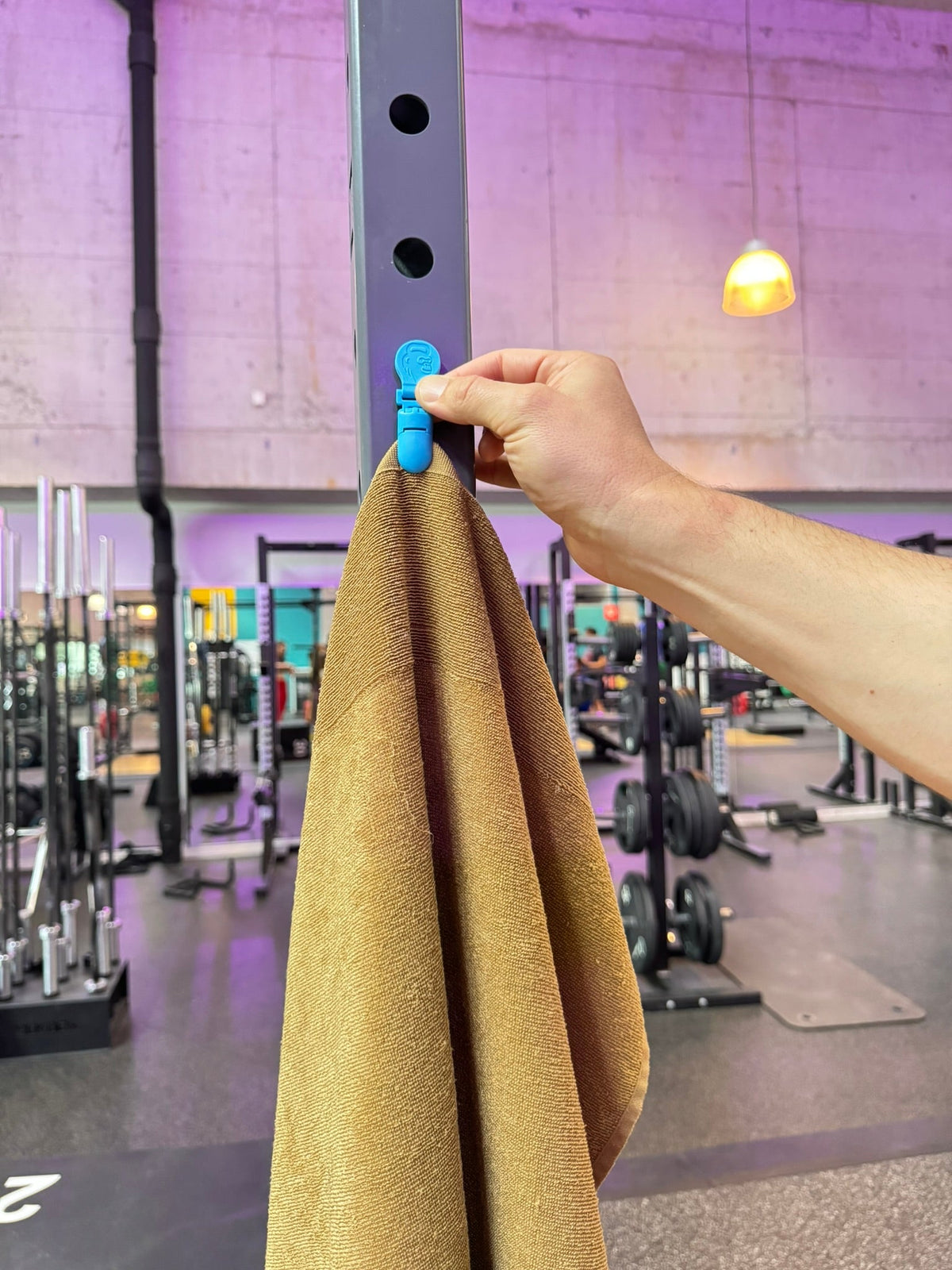 Hand befestigt ein Gym Handtuch mit einem magnetischen Handtuchclip am Stahlrahmen eines Racks im Fitnessstudio