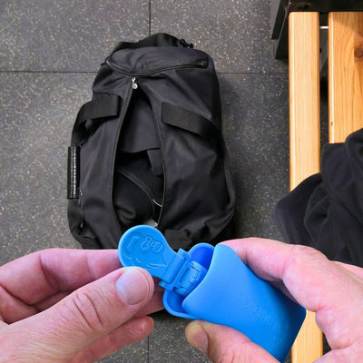 Blauer GYMMONKY Magnetic Towel Clip mit Silikon-Case vor einer Sporttasche im Gym.
