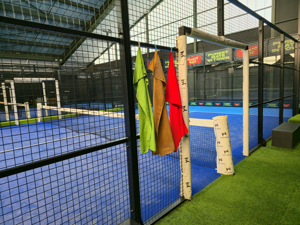 Tre asciugamani con Magnetic Towel Clips fissati alla rete di un campo da padel